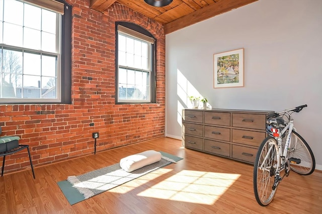 workout room with a wealth of natural light, light wood-style floors, wood ceiling, and brick wall