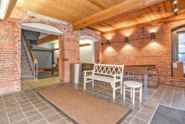 unfurnished dining area with stairway, beam ceiling, brick wall, and wooden ceiling