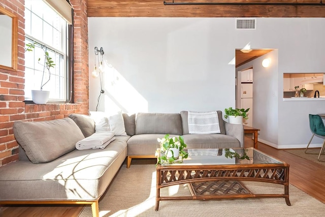 living area featuring visible vents, brick wall, baseboards, and wood finished floors