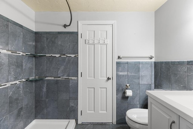 bathroom with tile walls, tiled shower, vanity, a textured ceiling, and toilet