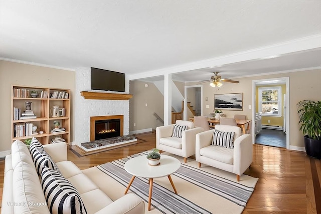 living room featuring a brick fireplace, wood-type flooring, ornamental molding, and baseboard heating