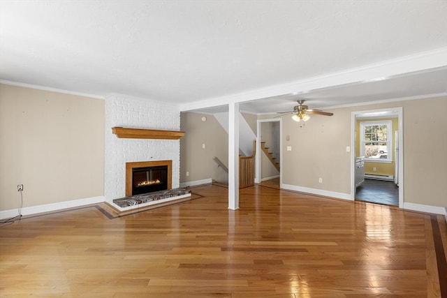 unfurnished living room with a brick fireplace, wood-type flooring, ornamental molding, and baseboard heating