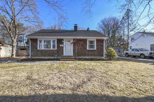 view of front of home featuring entry steps, a front lawn, roof with shingles, and a chimney