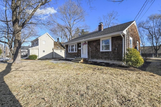 view of front facade with a front yard, roof with shingles, and a chimney