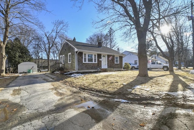 view of front of home featuring an outbuilding, a chimney, a shed, and aphalt driveway