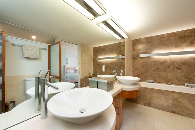 bathroom featuring tiled bath, tile patterned flooring, tile walls, and vanity