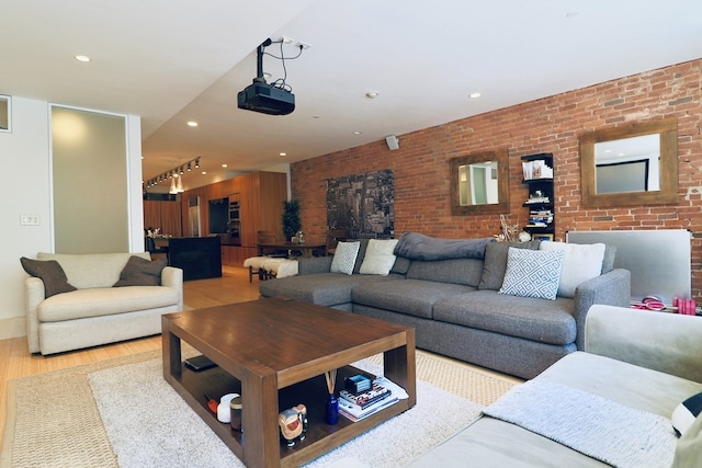 living room with rail lighting, brick wall, and light wood-type flooring