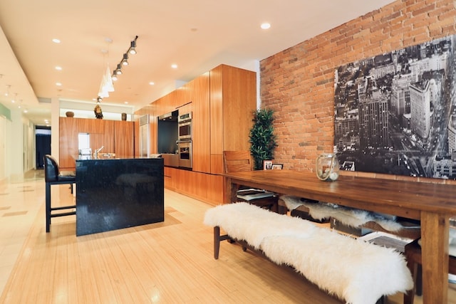 kitchen with a breakfast bar, brick wall, light hardwood / wood-style flooring, and stainless steel double oven