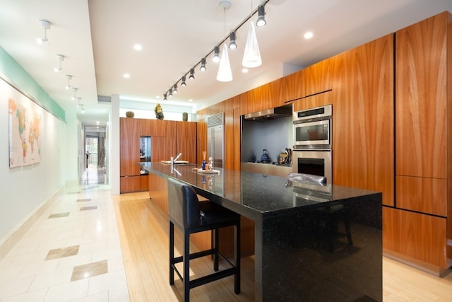 kitchen featuring a breakfast bar, a large island with sink, dark stone counters, and stainless steel appliances