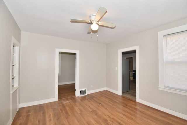 unfurnished bedroom with a spacious closet, wood finished floors, baseboards, ceiling fan, and a closet