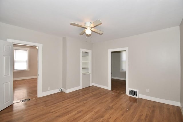 spare room featuring baseboards, a ceiling fan, wood finished floors, and built in shelves