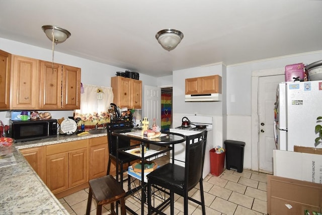 kitchen featuring black microwave, freestanding refrigerator, under cabinet range hood, light tile patterned floors, and a sink
