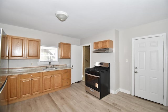 kitchen featuring stainless steel gas stove, a sink, under cabinet range hood, light wood-type flooring, and light countertops