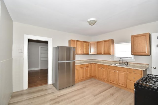 kitchen featuring freestanding refrigerator, a sink, black gas range oven, light countertops, and light wood-style floors
