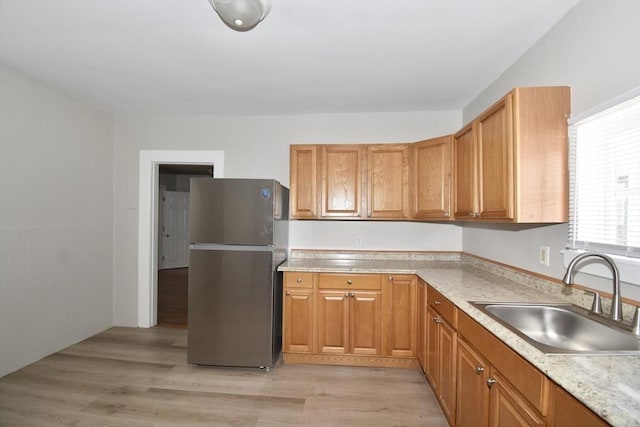 kitchen featuring freestanding refrigerator, a sink, light wood-type flooring, light countertops, and brown cabinets