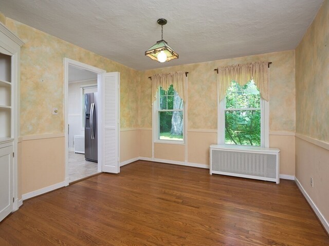 empty room featuring radiator, a textured ceiling, and wood-type flooring