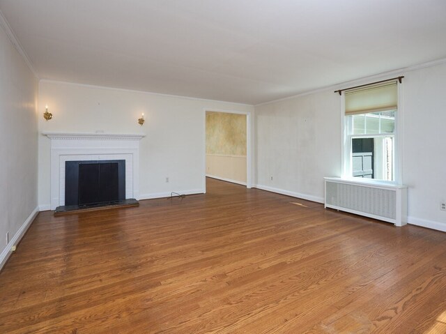 unfurnished living room with radiator heating unit, crown molding, hardwood / wood-style flooring, and a brick fireplace