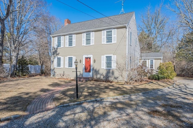 colonial inspired home with entry steps, fence, roof with shingles, a chimney, and a front yard