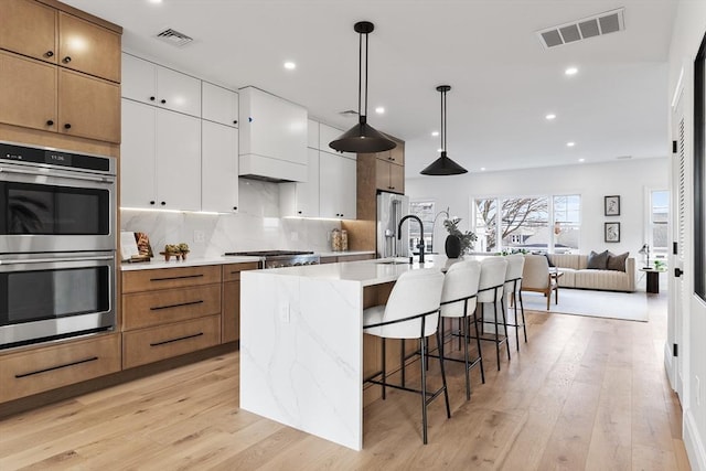 kitchen featuring pendant lighting, a kitchen island with sink, sink, appliances with stainless steel finishes, and white cabinetry