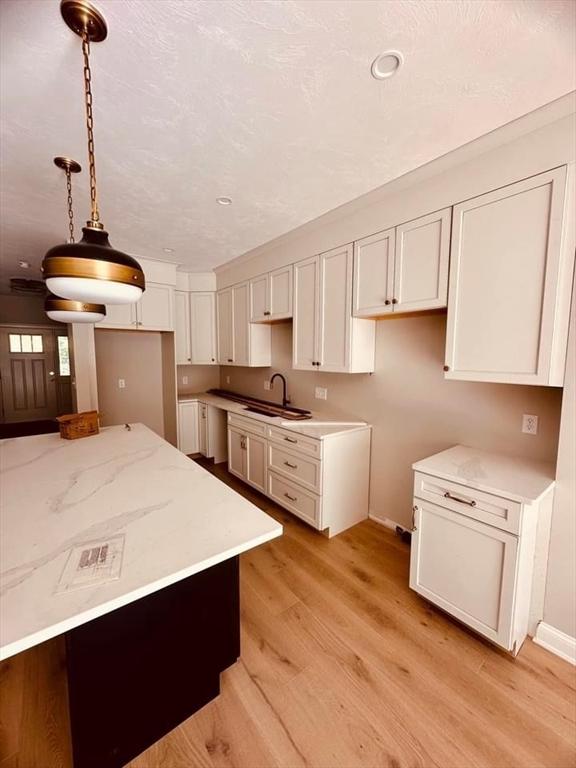 kitchen featuring white cabinets, sink, decorative light fixtures, light hardwood / wood-style floors, and light stone counters