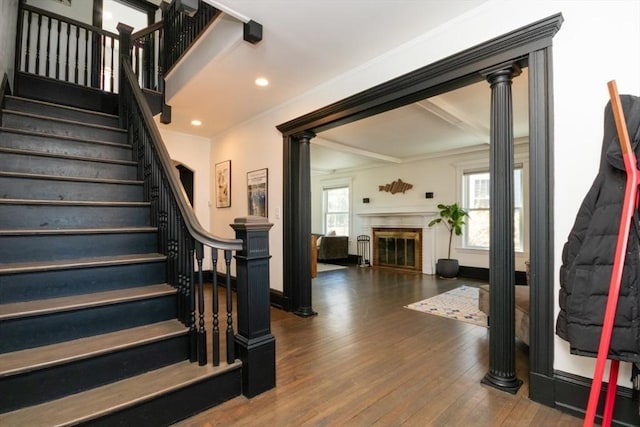 stairway featuring crown molding, a glass covered fireplace, recessed lighting, decorative columns, and wood finished floors