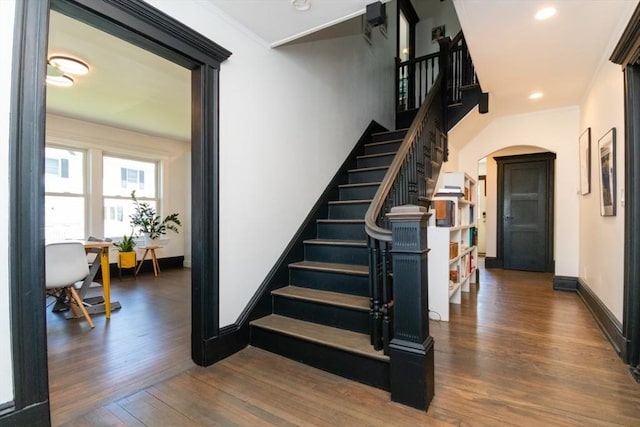 stairway with baseboards, arched walkways, wood finished floors, and ornamental molding