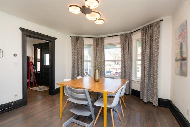 dining space featuring baseboards, dark wood finished floors, crown molding, and a notable chandelier