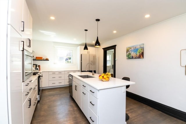 kitchen with appliances with stainless steel finishes, a sink, light countertops, an island with sink, and dark wood-type flooring