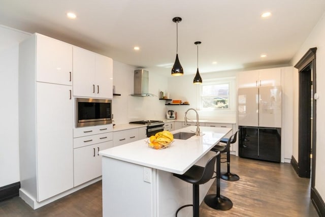 kitchen featuring a kitchen bar, appliances with stainless steel finishes, a sink, dark wood-style floors, and wall chimney exhaust hood
