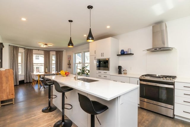 kitchen featuring appliances with stainless steel finishes, a sink, light countertops, wall chimney exhaust hood, and a kitchen bar