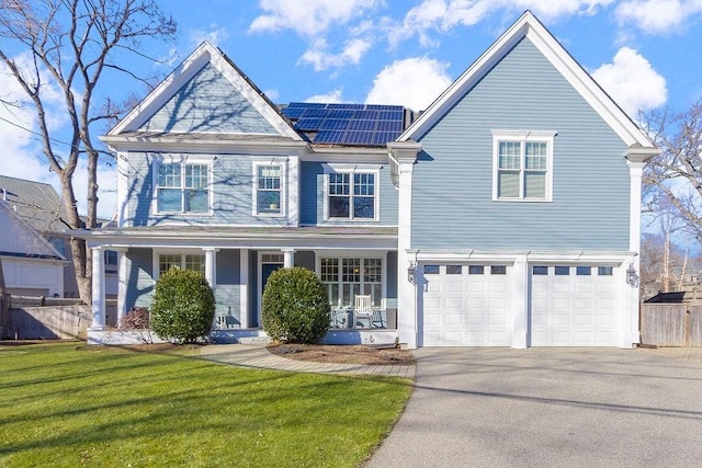 view of front of house with driveway, a porch, fence, roof mounted solar panels, and a front lawn