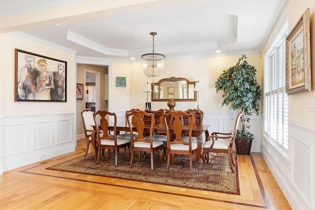 dining room featuring light wood finished floors, ornamental molding, a raised ceiling, and wainscoting