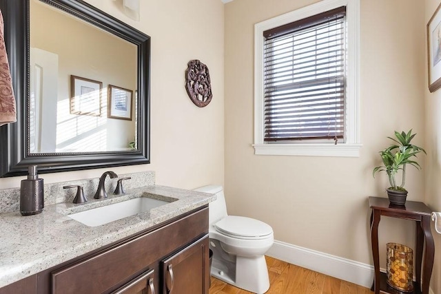 half bathroom with baseboards, vanity, toilet, and wood finished floors