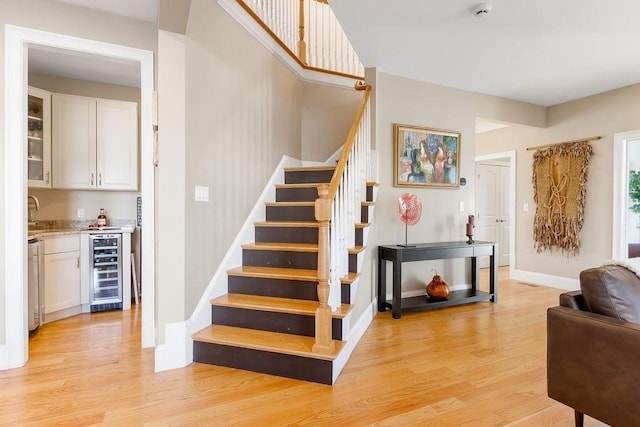 stairway with baseboards, wine cooler, wood finished floors, and wet bar