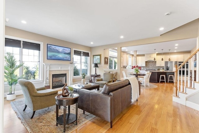 living area featuring light wood-type flooring, a glass covered fireplace, recessed lighting, and stairs