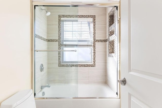 bathroom featuring toilet and combined bath / shower with glass door