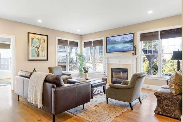 living area featuring a healthy amount of sunlight, light wood finished floors, baseboards, and a tile fireplace