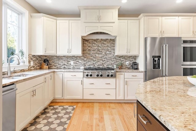 kitchen featuring decorative backsplash, light stone counters, appliances with stainless steel finishes, light wood-type flooring, and a sink