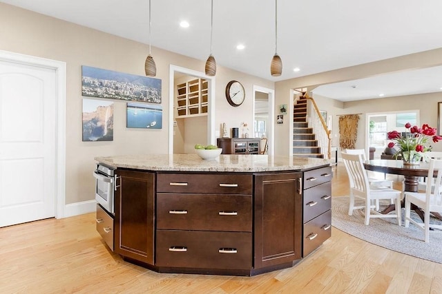 kitchen featuring dark brown cabinets, hanging light fixtures, light wood-style flooring, and light stone countertops