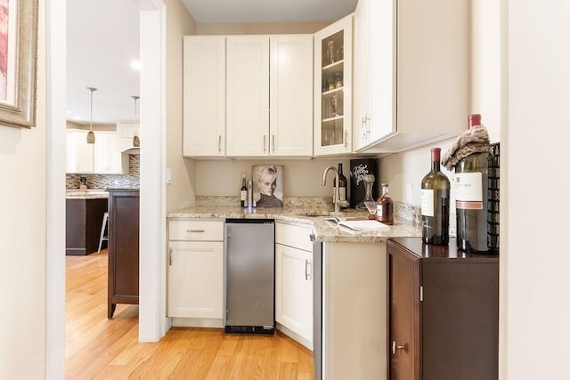 kitchen featuring light stone counters, white cabinetry, a sink, and light wood finished floors