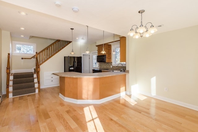 kitchen with backsplash, black appliances, an inviting chandelier, sink, and light wood-type flooring