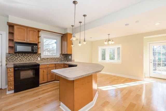 kitchen featuring hanging light fixtures, light wood-type flooring, black appliances, and plenty of natural light