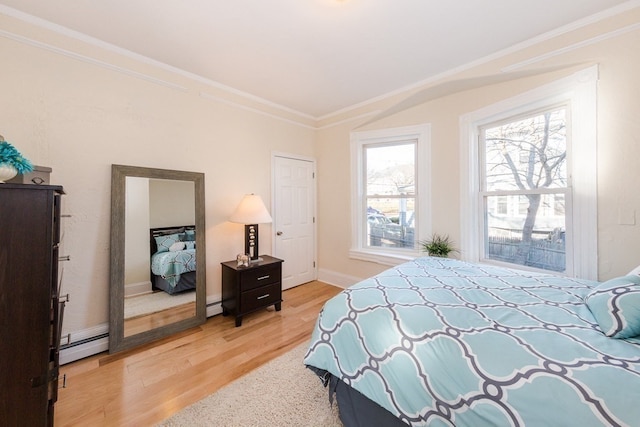 bedroom with ornamental molding, a baseboard heating unit, light hardwood / wood-style floors, and multiple windows