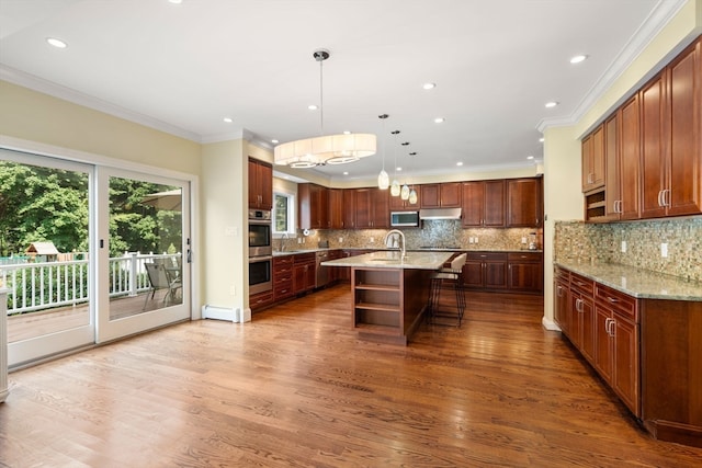 kitchen with tasteful backsplash, a kitchen island with sink, wood-type flooring, a kitchen bar, and decorative light fixtures