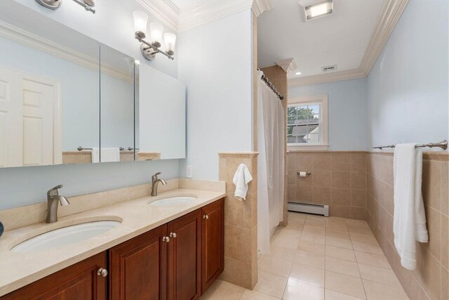 bathroom with a baseboard radiator, double vanity, tile patterned flooring, tile walls, and crown molding