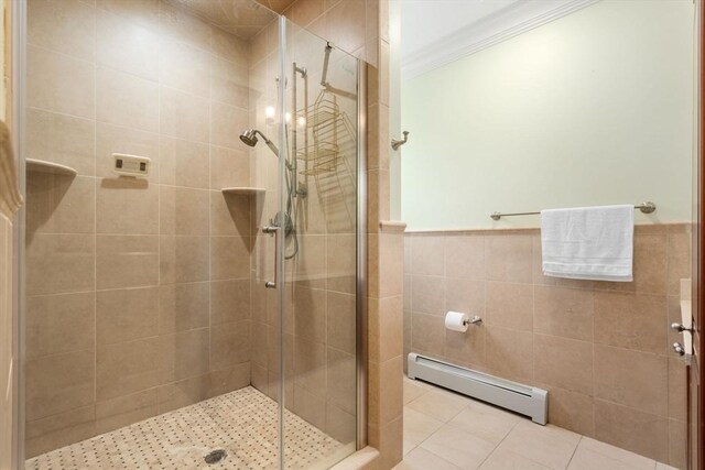 bathroom featuring ornamental molding, a baseboard radiator, a shower with shower door, tile patterned flooring, and tile walls