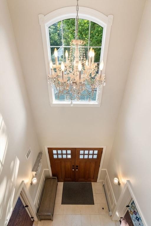 foyer featuring light tile patterned floors, visible vents, baseboards, a towering ceiling, and an inviting chandelier