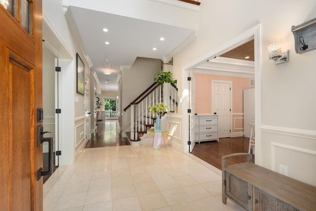 foyer featuring crown molding, a wainscoted wall, stairs, and a decorative wall