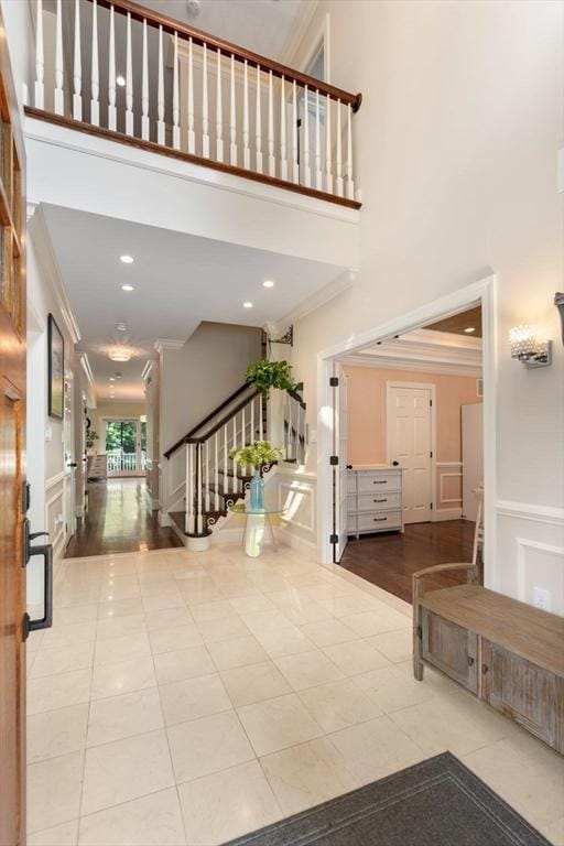 foyer entrance with stairs, a decorative wall, a towering ceiling, ornamental molding, and tile patterned floors