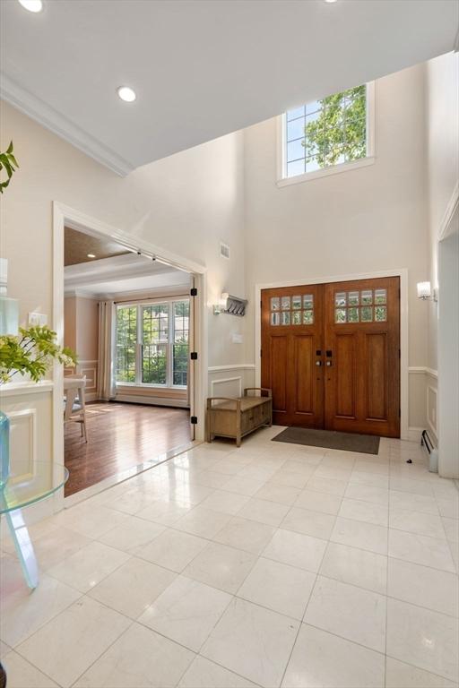 entryway featuring baseboard heating, light hardwood / wood-style floors, a high ceiling, and ornamental molding